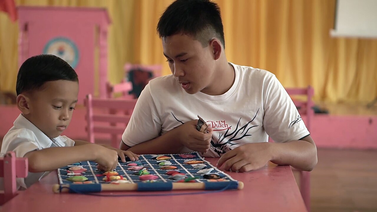 Seorang pendamping menemani anak menyusun kepingan permainan di meja