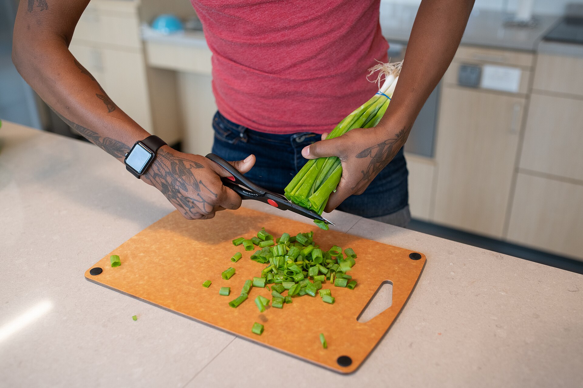 Seseorang memotong daun bawang memakai gunting dapur yang mudah digenggam