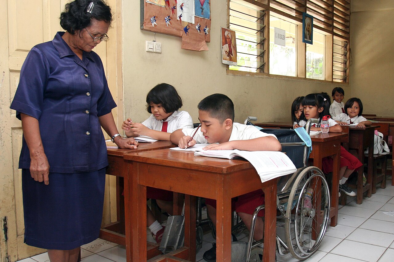Guru mendampingi murid pengguna kursi roda di ruang kelas